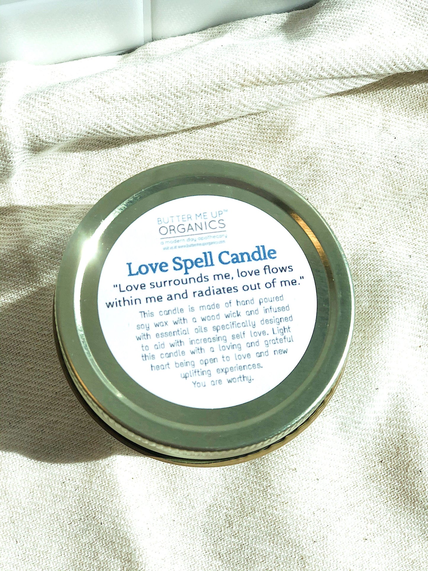 love spell intention candle is 4 oz of hand-poured soy wax in a glass jar with a metal lid closed "love surrounds me, love flows within me and raiates out of me." this candle is made of hand poured soy wax with a wood wick and infused with essential oils speifically desidgned to aid with improving self love. light this candle with a loving and grateful heart being open to love uplifting experiences. you are worthy." butter me up organics a modern day apothecary